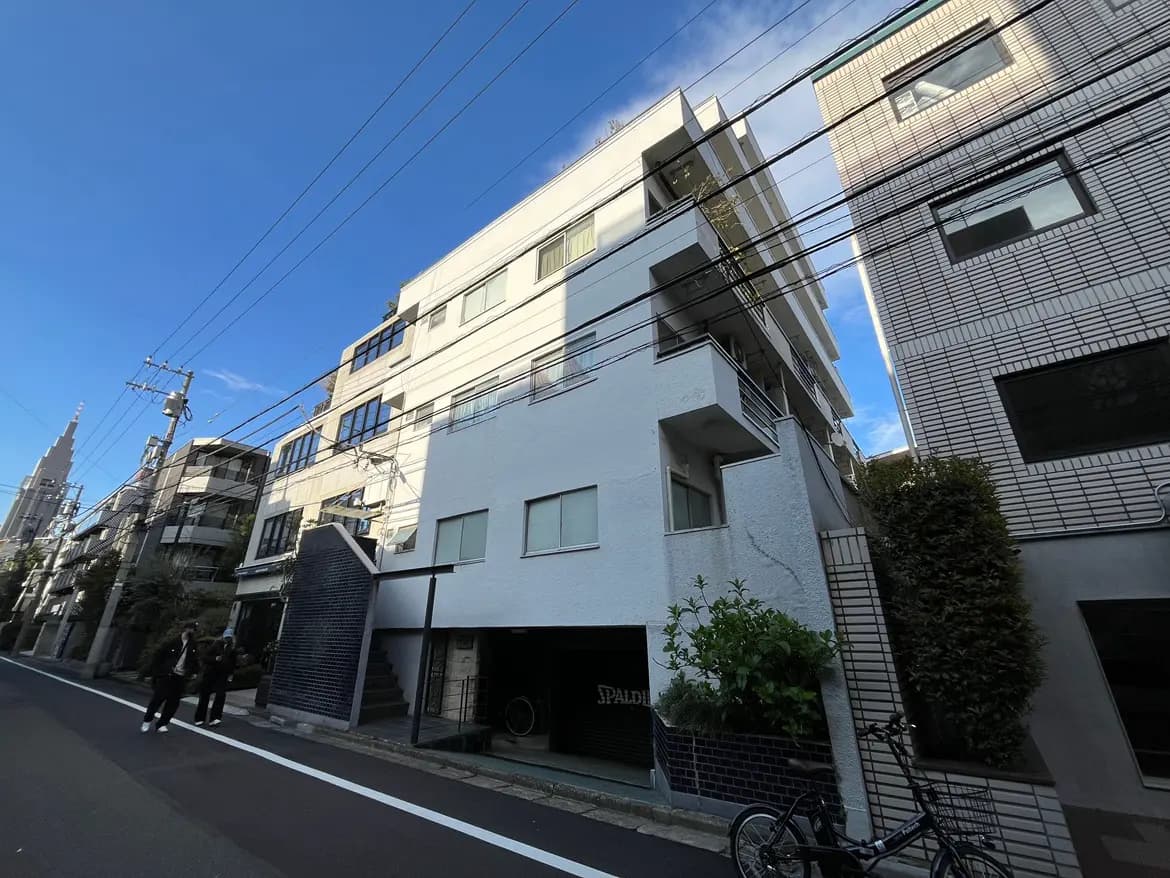 - 都市的な環境にある現代的なアパートメントビル、青い空と電線が見える風景、歩道にいる人々と自転車のあるシーン