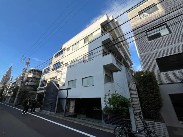 - 都市的な環境にある現代的なアパートメントビル、青い空と電線が見える風景、歩道にいる人々と自転車のあるシーン
