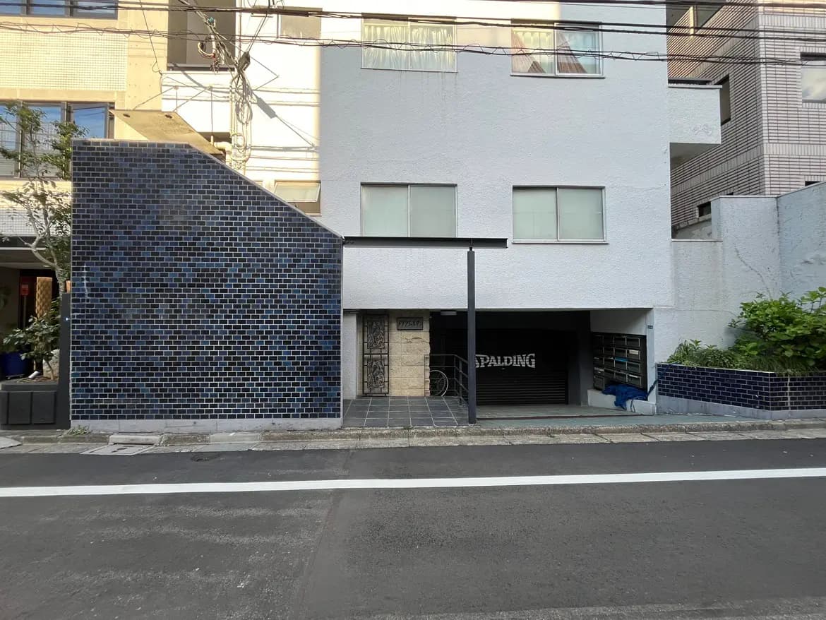 - モダンな外観の建物、青いタイルで装飾された壁と白い外壁、シャッター付きのガレージと周囲の緑があるエントランス