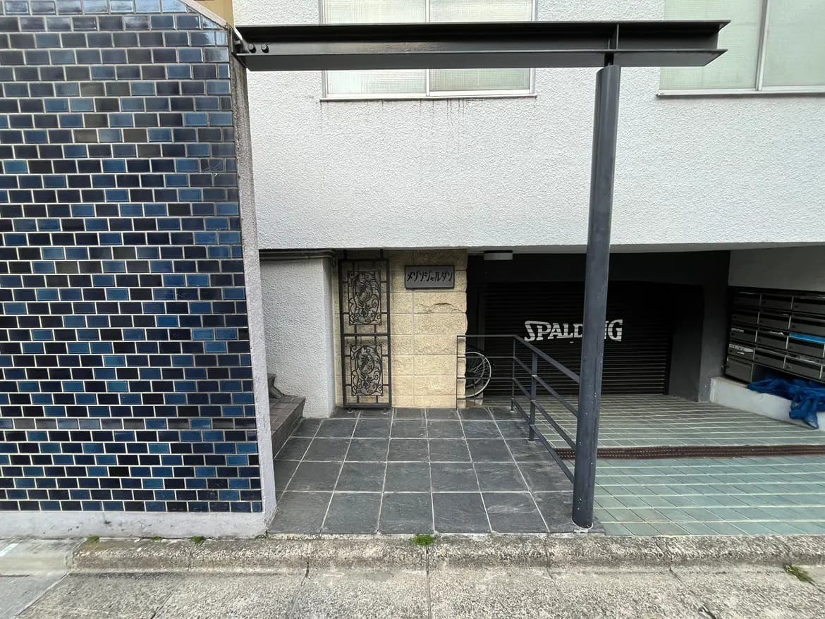 - 石造の入り口と黒いタイルのアプローチ、青いタイルの壁が特徴の現代的な建物の外観