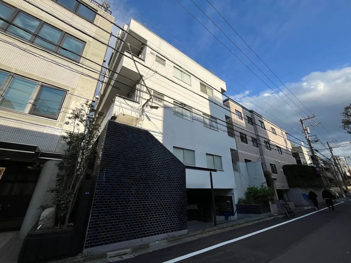 - 都市の風景に立つ現代的な集合住宅、白とグレーの外観、近くの通りを歩く人々と青空の背景