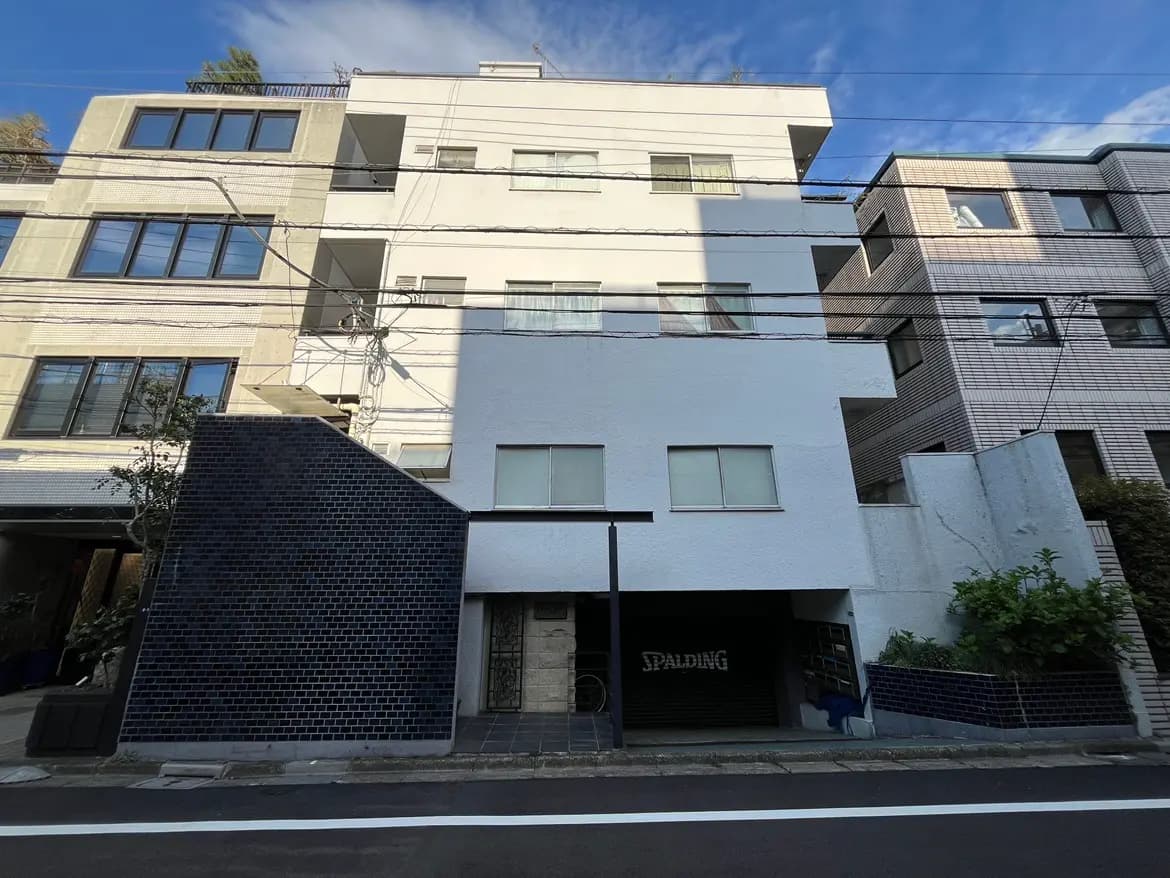 - モダンなデザインの集合住宅、白い外壁に黒いタイルのアクセント、明るい空の下にある建物の外観
