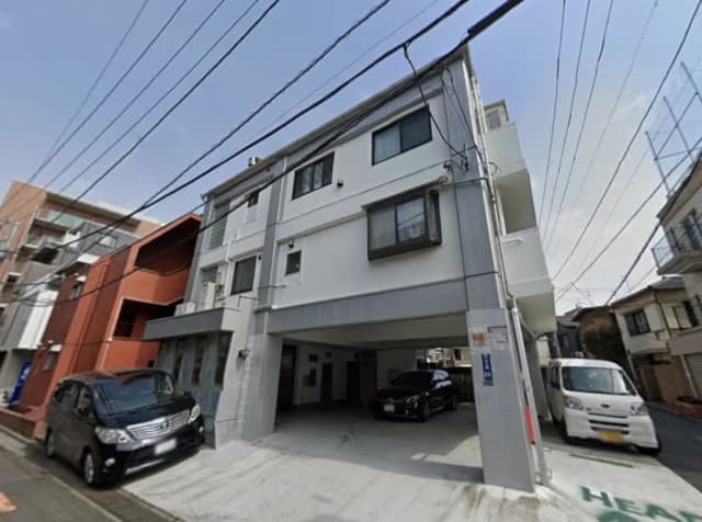 - 白い外観の複合住宅、地下駐車場付き、周囲には他の住宅が点在する街の風景