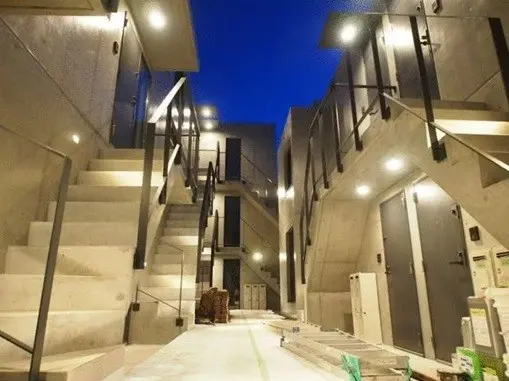 - モダンなコンクリートの建物内階段、明るい照明が施されたエントランス、夜空を背景にしたシャープなデザインのインテリア