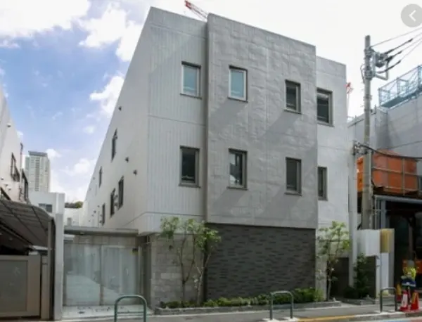 - シンプルでモダンなデザインの外観を持つ3階建ての建物、明るい空と周囲の緑に囲まれた様子