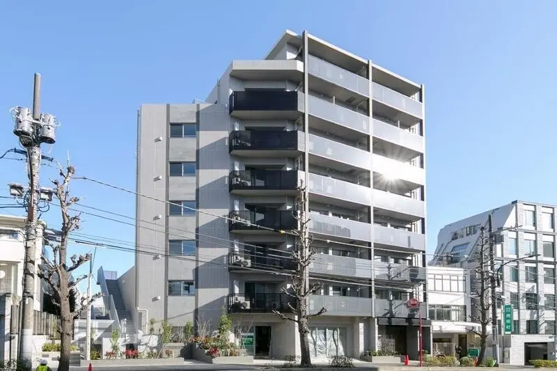 - 明るい青空の下に立つ現代的なデザインのマンション、周囲に電柱と剪定された木々が見える景観