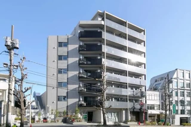 - 明るい青空の下に立つ現代的なデザインのマンション、周囲に電柱と剪定された木々が見える景観