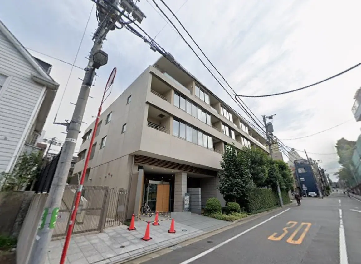 - モダンな外観のマンション入り口、周囲には交通標識や緑の植栽があり、周辺道路が写る景観