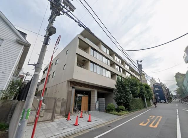 - モダンな外観のマンション入り口、周囲には交通標識や緑の植栽があり、周辺道路が写る景観