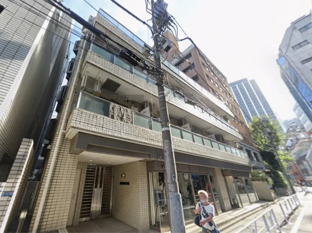 - 都市の中心に位置するモダンなマンションの外観、ガラスバルコニーとデザインされたエントランス、周囲に高層ビルが立ち並ぶシーン