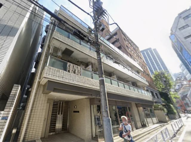 - 都市の中心に位置するモダンなマンションの外観、ガラスバルコニーとデザインされたエントランス、周囲に高層ビルが立ち並ぶシーン