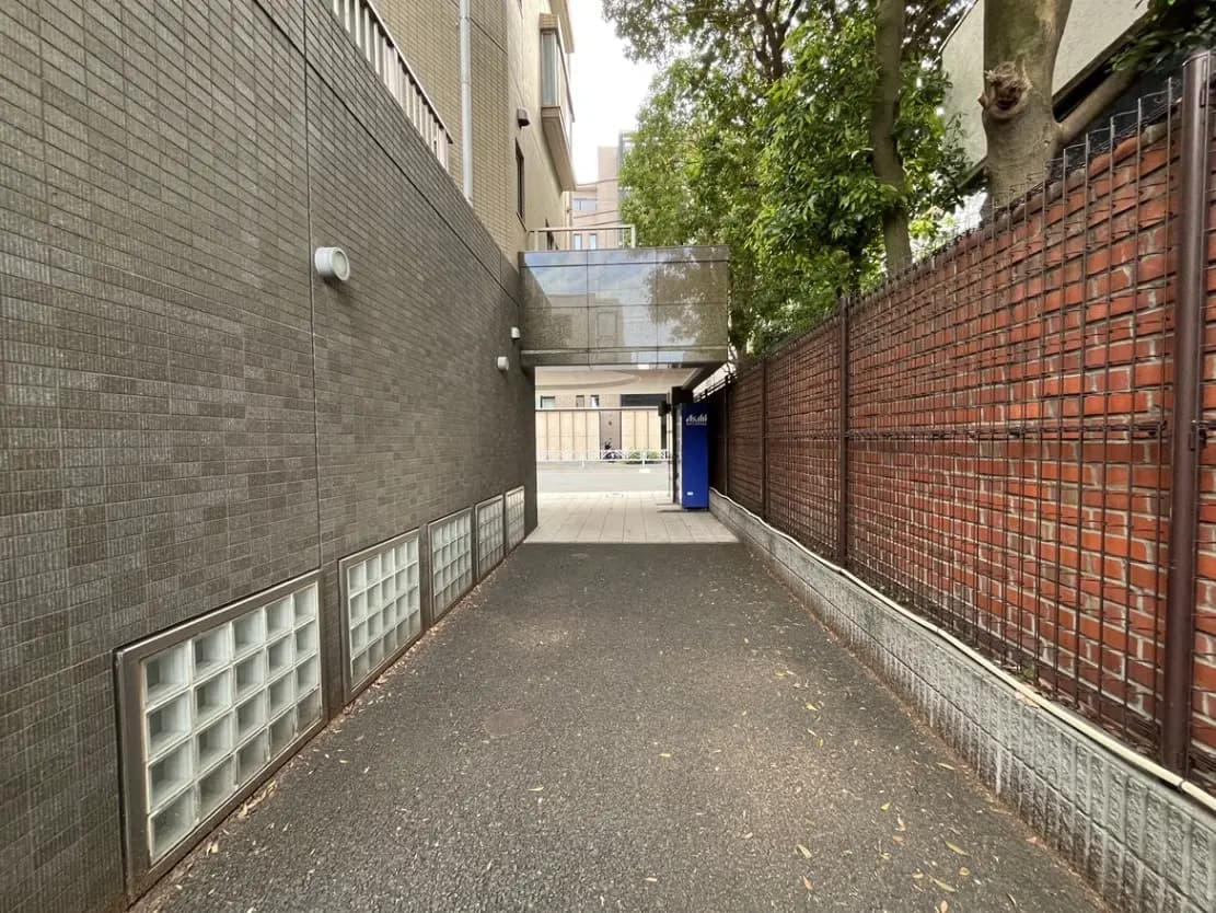 - コンクリートの壁に囲まれた狭い通路、ガラスブロックの窓とレンガで作られたフェンスが特徴的な風景