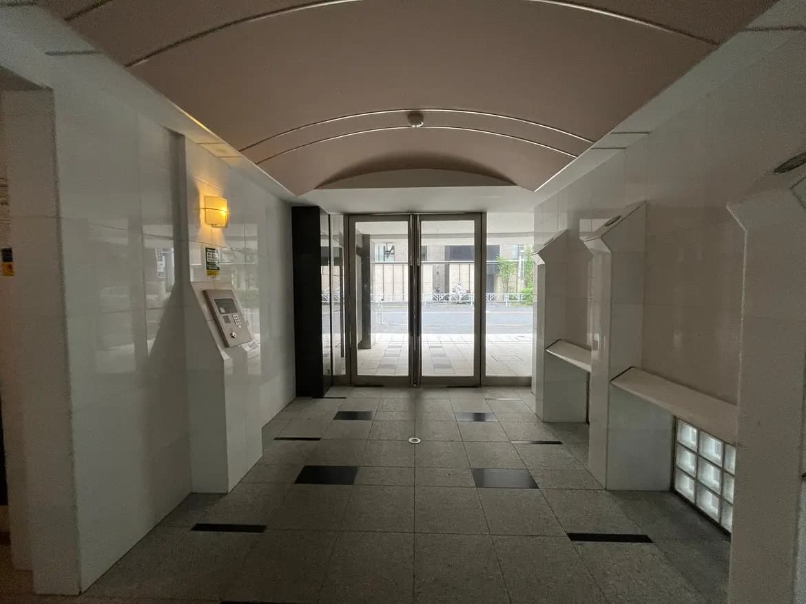 - モダンなエントランスホール、白いタイルの壁と床、照明、インターフォンが設置された入り口の内部デザイン