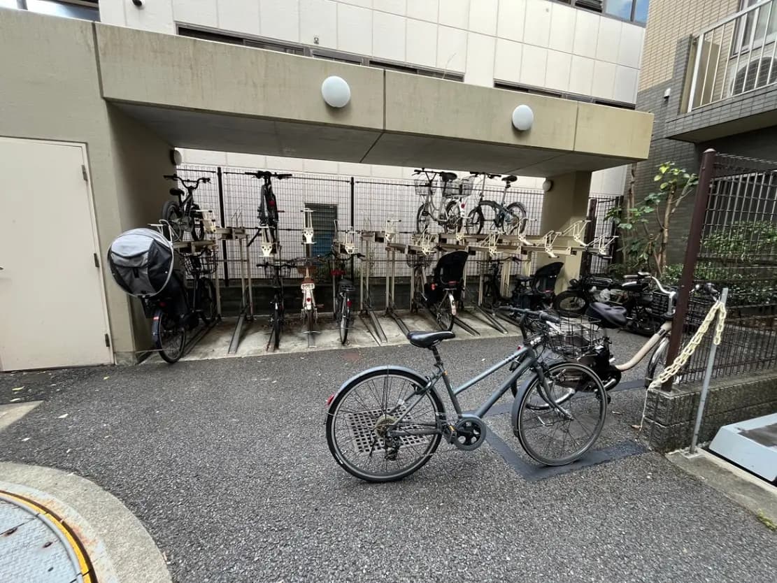 - 自転車置き場の風景、様々なタイプの自転車が停められた屋根付きのスペース、手前には灰色の自転車がある