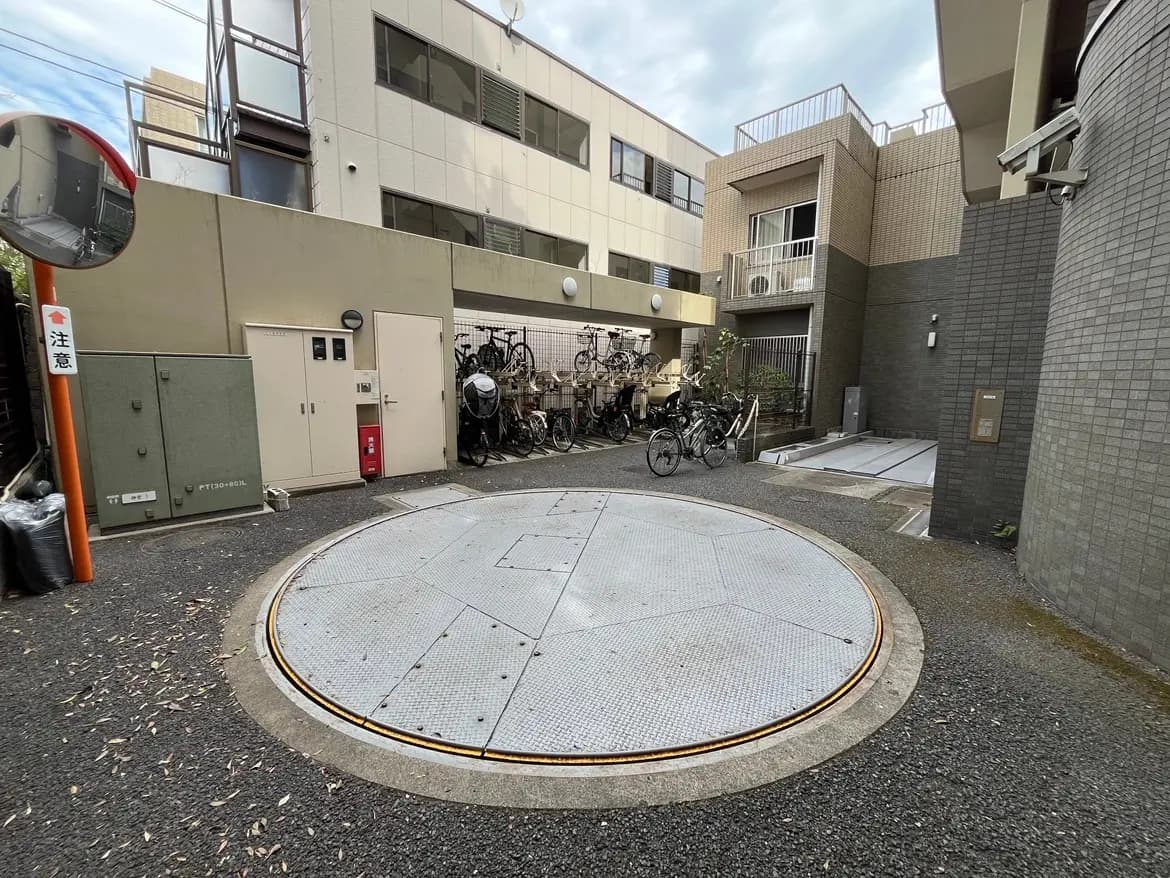 - 自転車が停められた裏庭の回転式駐輪場、周囲に建物と注意看板が見える風景
