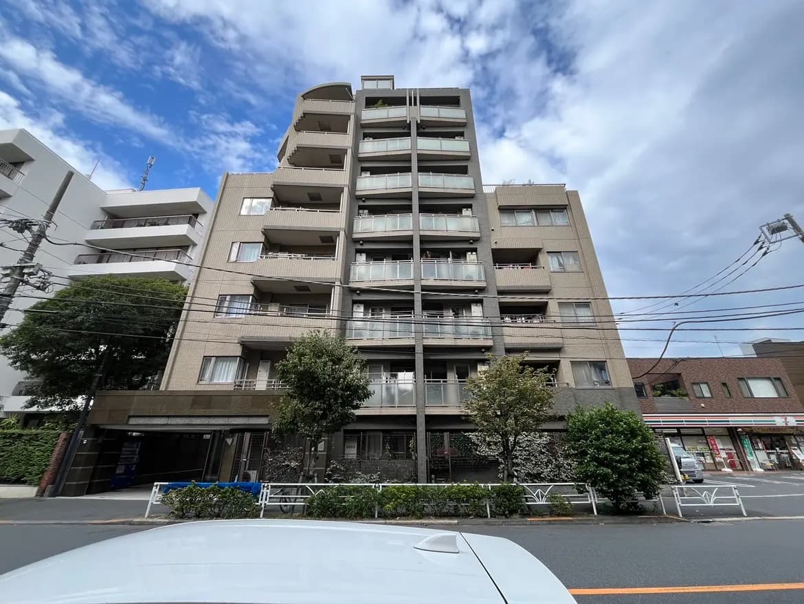 - 都市部に位置する近代的な6階建てマンション、窓にバルコニーがあり、周囲の緑や店舗が見える景観