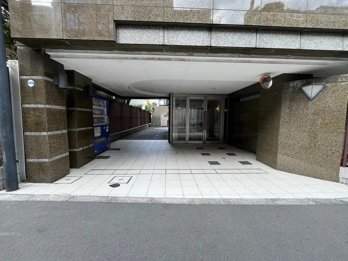 - モダンなビルのエントランス、ガラスの扉と石材の壁、横には自動販売機が並んでいる通路