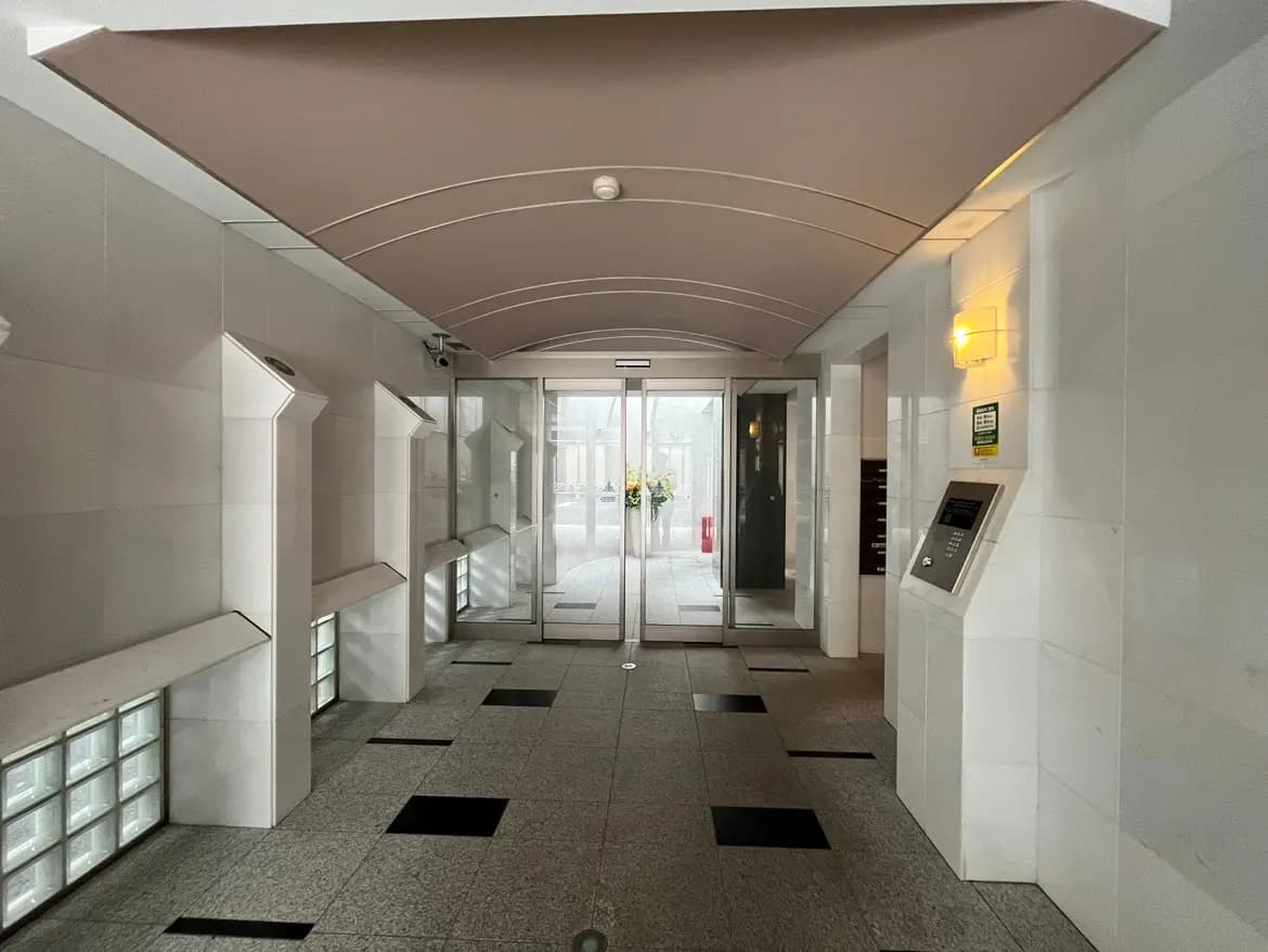 - モダンなエントランスホール、明るい照明とガラスブロックの壁、背景に自動ドアと郵便受けが見えるインテリア