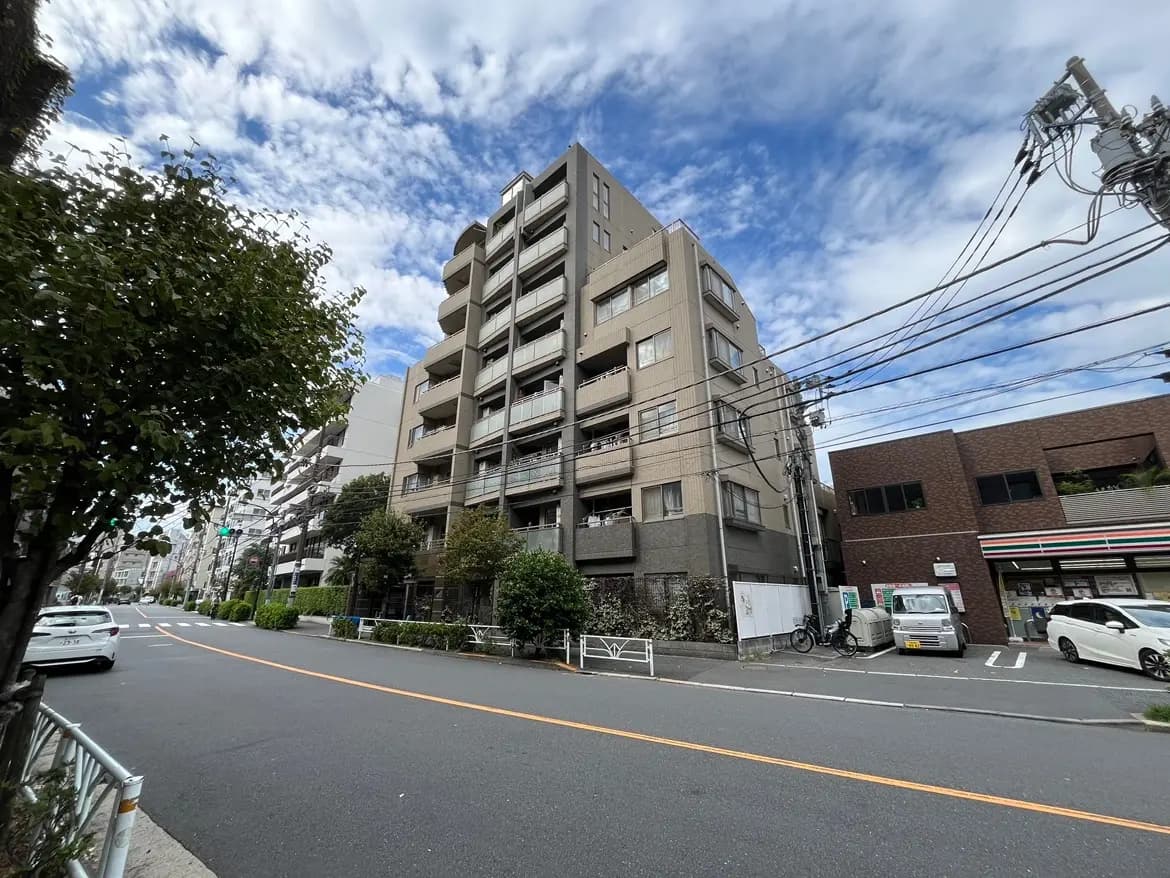 - 近代的なマンションが立ち並ぶ都会の風景、青空と雲が広がる、道路沿いの植栽と車両が見える景色