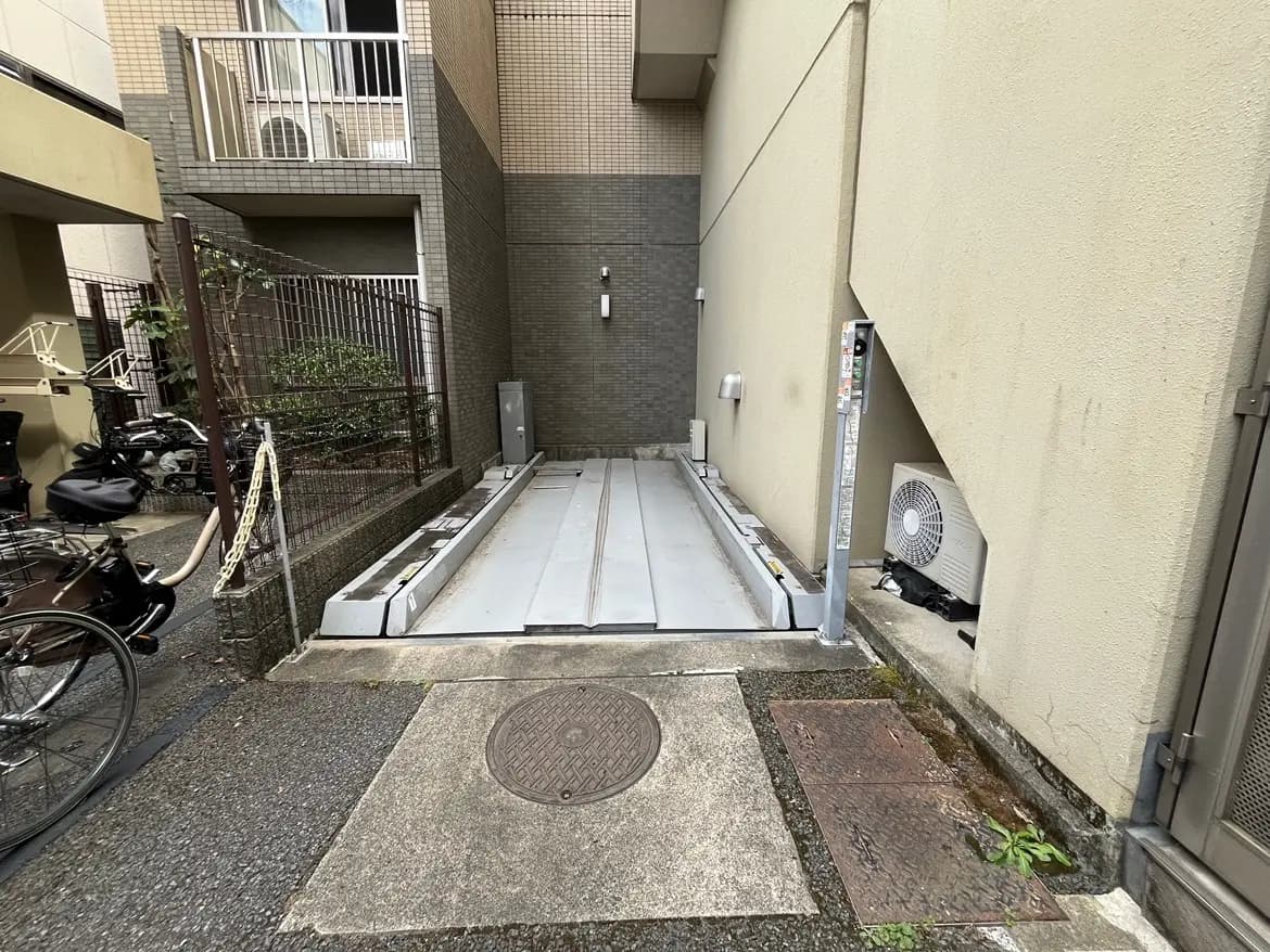 - 駐輪スペースのないマンションの外観、ステンレス製のスロープと隣接するバイク置き場、周囲に緑の植物が見える景観