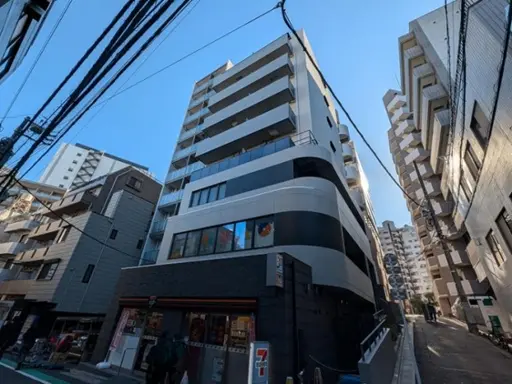 - 近代的なマンションの外観、隣接する建物との対比、周囲の都会的な風景と青空が広がるシーン