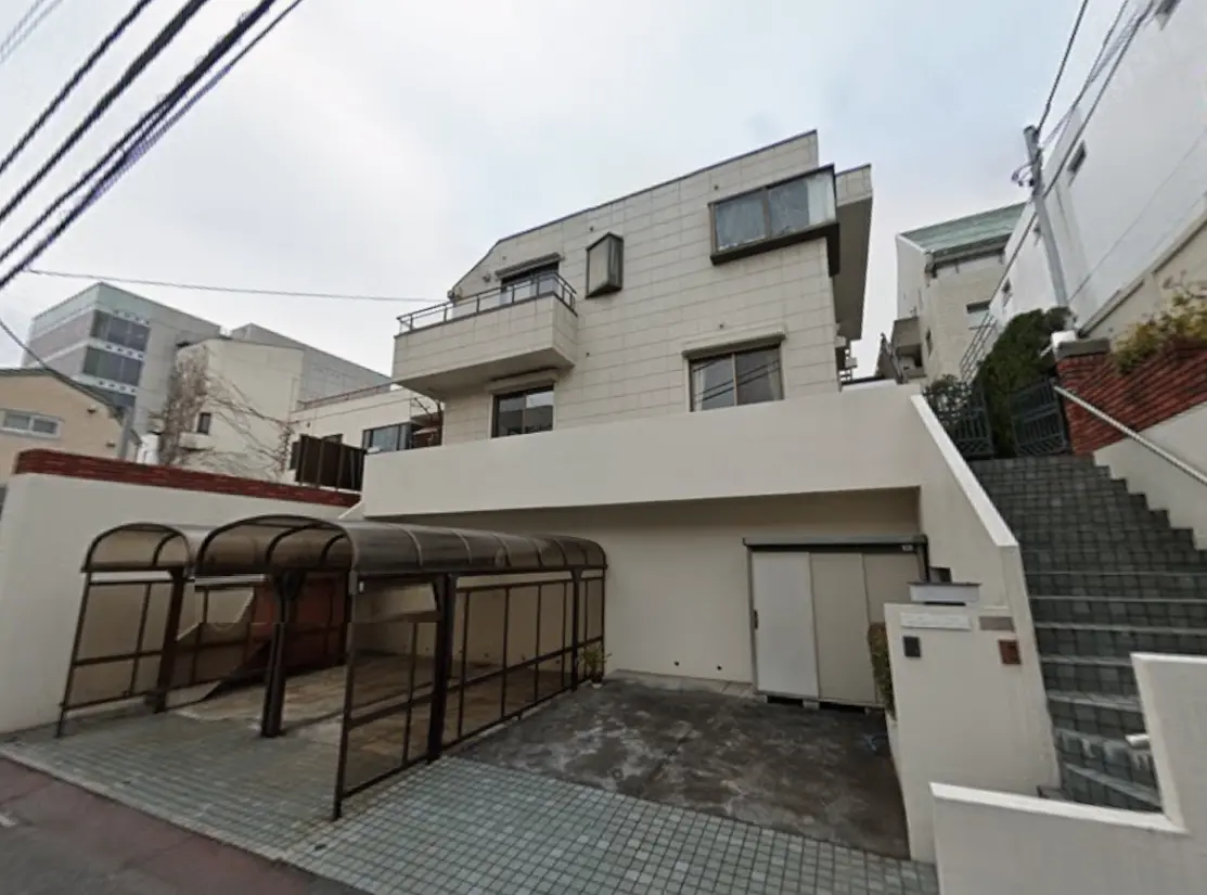 - モダンな外観の家とその前にある屋根付き駐車スペース、周囲に階段と植栽がある景観