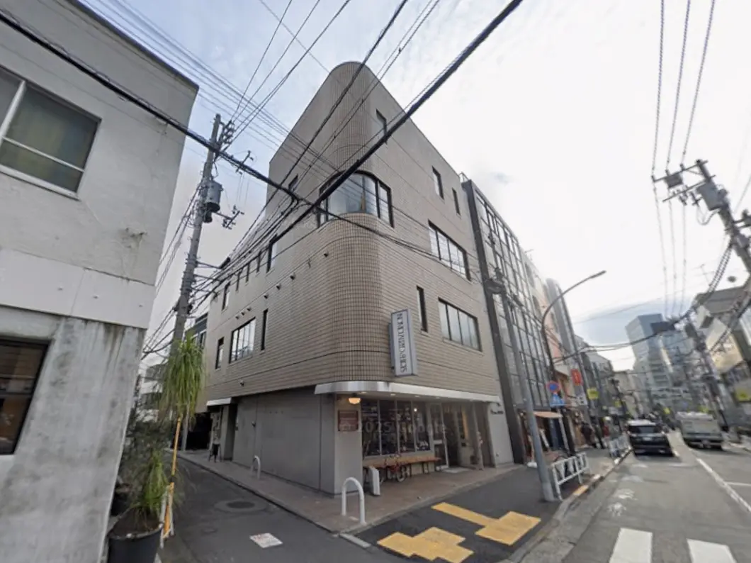 - 角地に建つ現代的な商業ビル、窓が多く明るい外観、周辺の街並みや電柱が見える風景