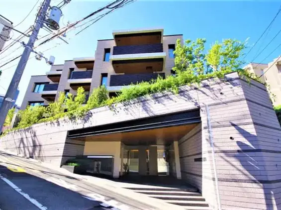 - 緑豊かな景観を持つモダンなマンションの外観、周囲には高い植栽と整備されたエントランスが特徴の風景