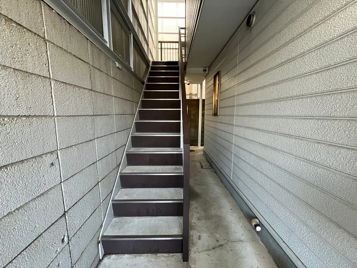 - 外に面した階段、コンクリート製の床とスチール製の手すり、ライトグレーの壁のある住宅の通路