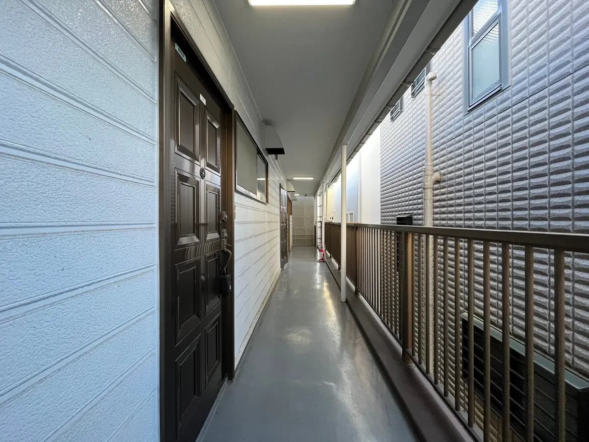 - 明るい照明が特徴の長い廊下、両側に並ぶドアとシンプルな内装、壁には白い壁材が使用されたアパートの内部風景