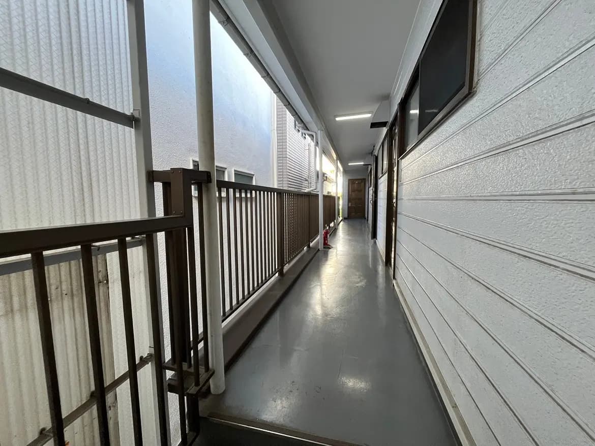 - 明るい廊下の通路、白い壁と手すりがある、隣接する部屋のドアが並ぶアパートの内部風景