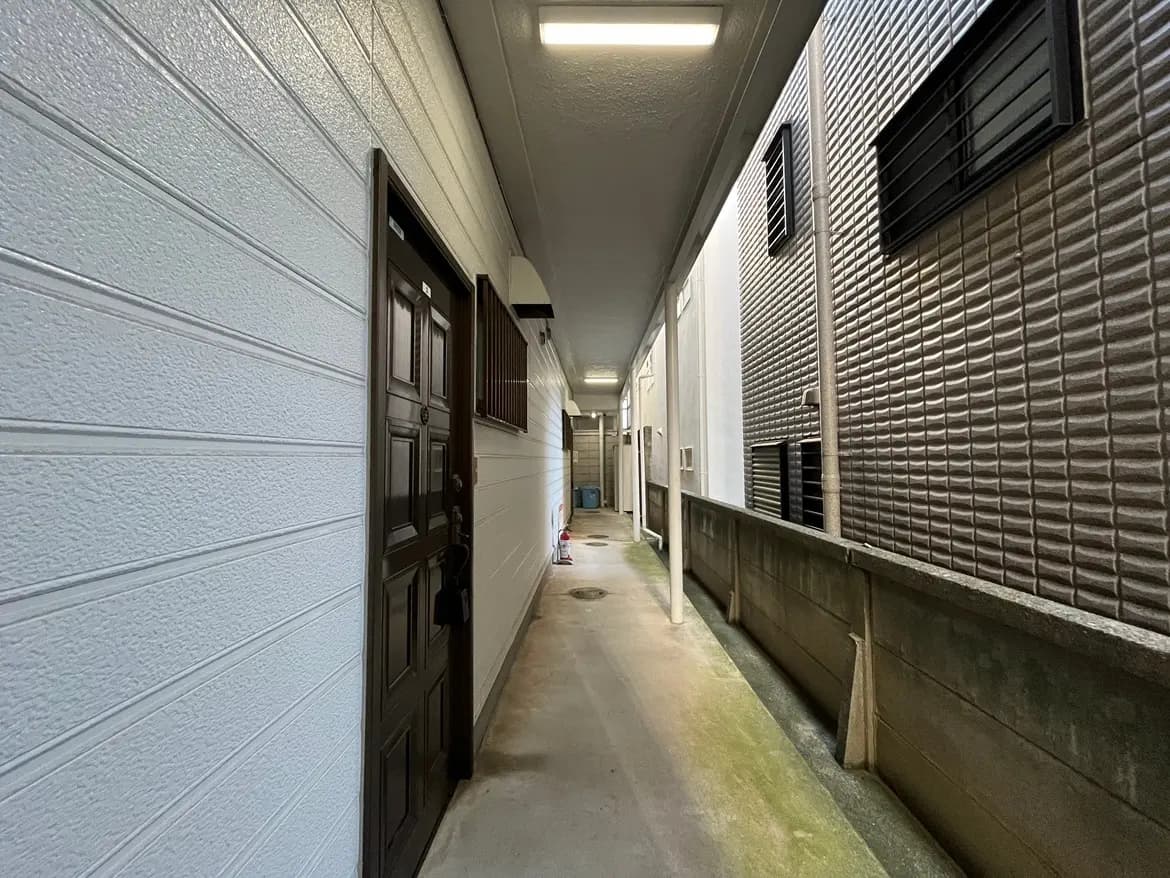 - 建物の外通路、白い壁と茶色のドア、狭いスペースに隣接した住居の外観