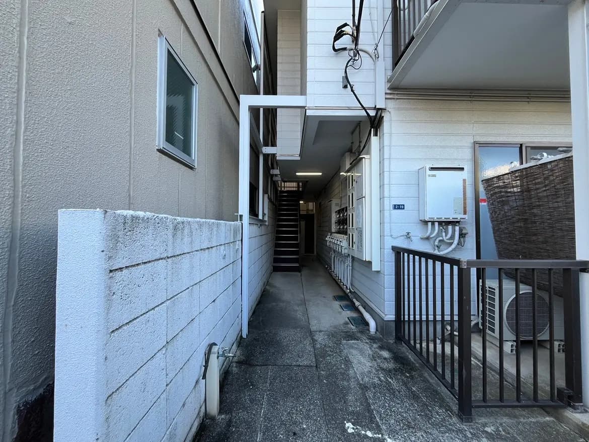 - アパートの外観の通路、白い壁と窓、階段、電気メーターが並ぶエリアの風景