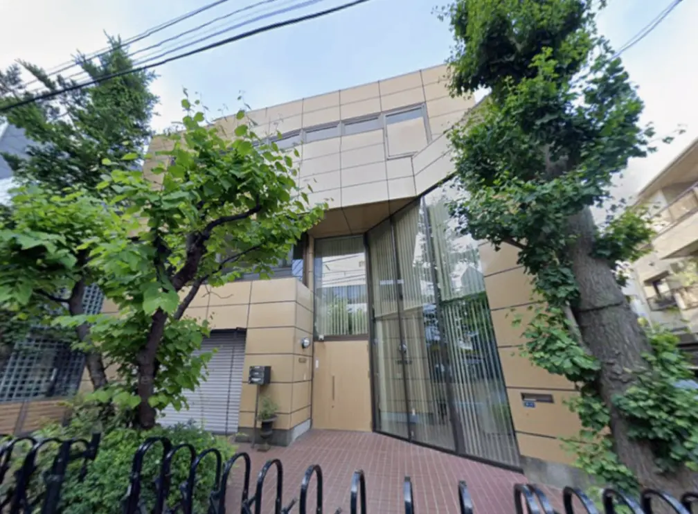 - モダンな外観の建物、ガラス張りのエントランスと緑豊かな木々に囲まれた景観、整然としたアプローチが特徴