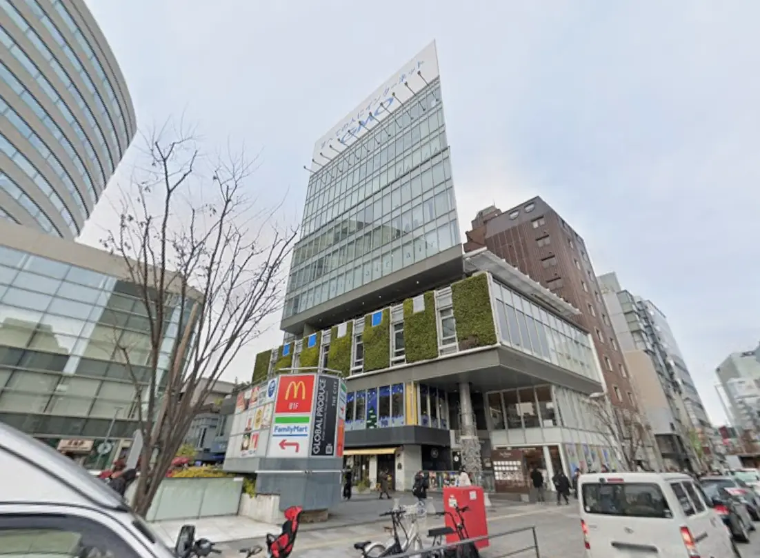 - 現代的な商業ビルの外観、ガラス張りのファサードと緑のアクセント、1階にマクドナルドとファミリーマートの看板が見える