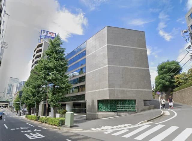 - 現代的なデザインの商業ビル、ガラス窓が特徴的で周囲に緑豊かな街路樹がある風景