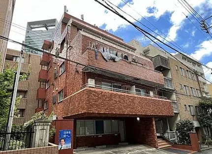 - 赤レンガ造りの外観が特徴的なマンション、周囲には高層ビルが立ち並ぶ都市景観、洗濯物が干されたバルコニーと青空が広がる風景