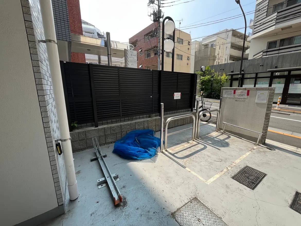 - 都市のエントランスエリア、黒いフェンスと青いシート、大きな窓のある建物の外観、周囲には自転車と電線が見える風景
