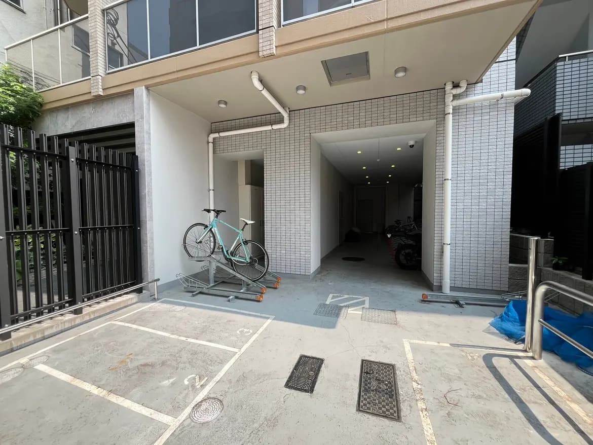 - 自転車スタンドに置かれた青い自転車、ガレージの入口、モダンな外観の建物と整然とした駐車スペースの風景