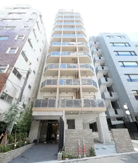 新築マンションの外観写真、ベージュの壁とガラスのバルコニー、周囲には高層建築物が立ち並ぶ都市風景