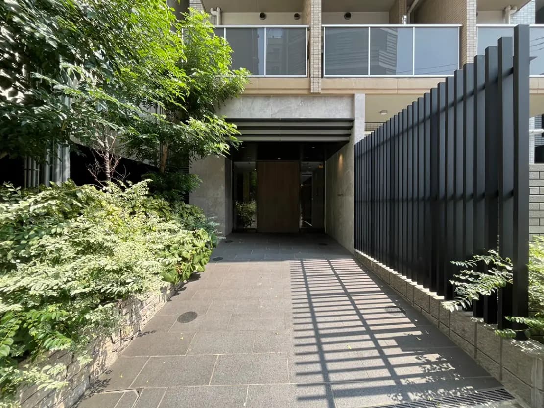 緑豊かな植栽に囲まれたモダンなエントランス、自然光が差し込むアプローチとスタイリッシュなファサード