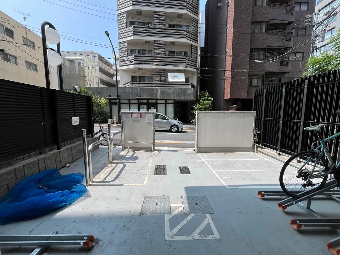 - 自転車置き場の様子、周囲に高い建物が立ち並び、晴れた日の青空と明るい照明が映るエリア