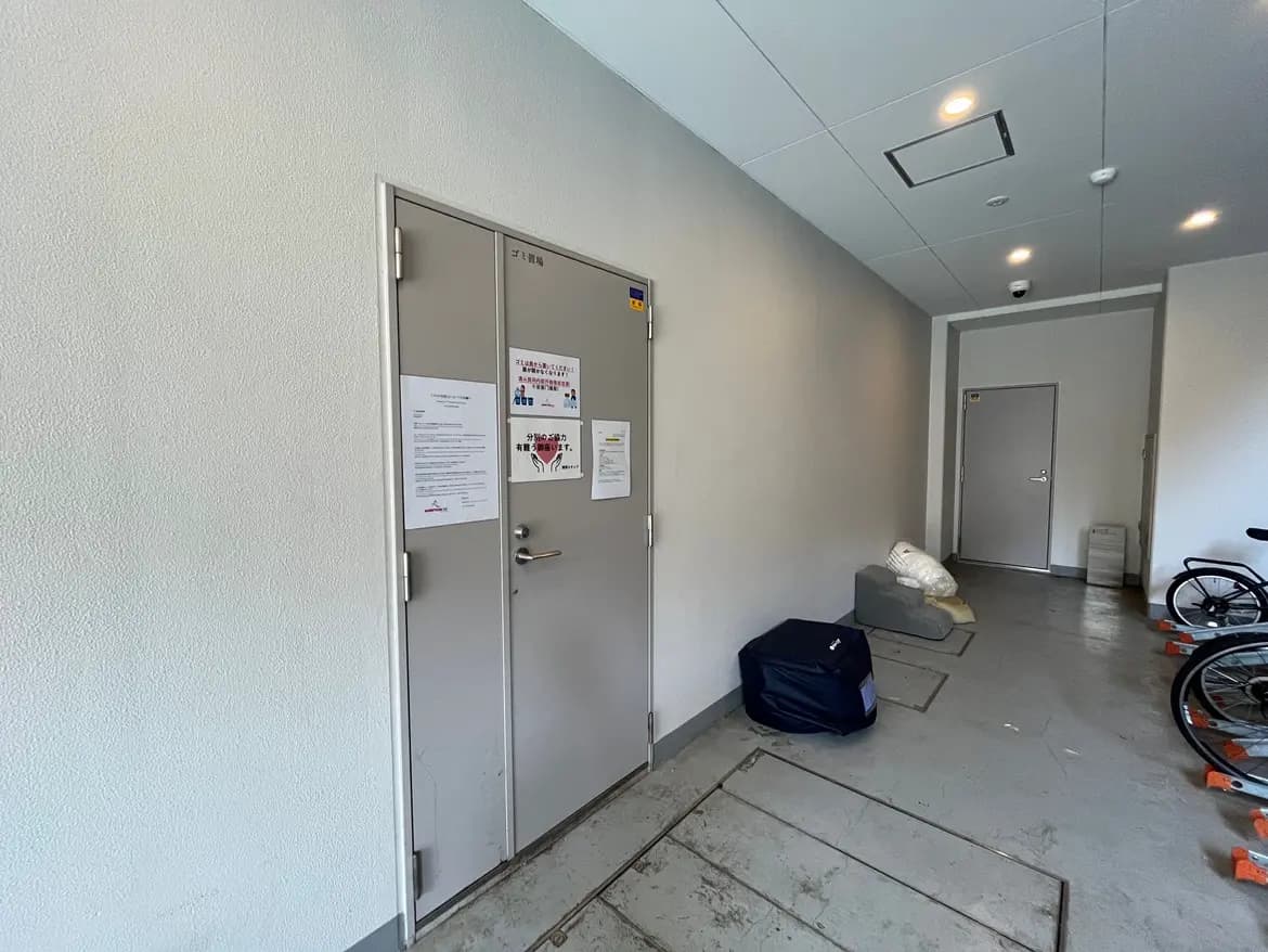 - 自転車置き場と無地の壁、掲示物が貼られた扉がある整然とした廊下の様子
