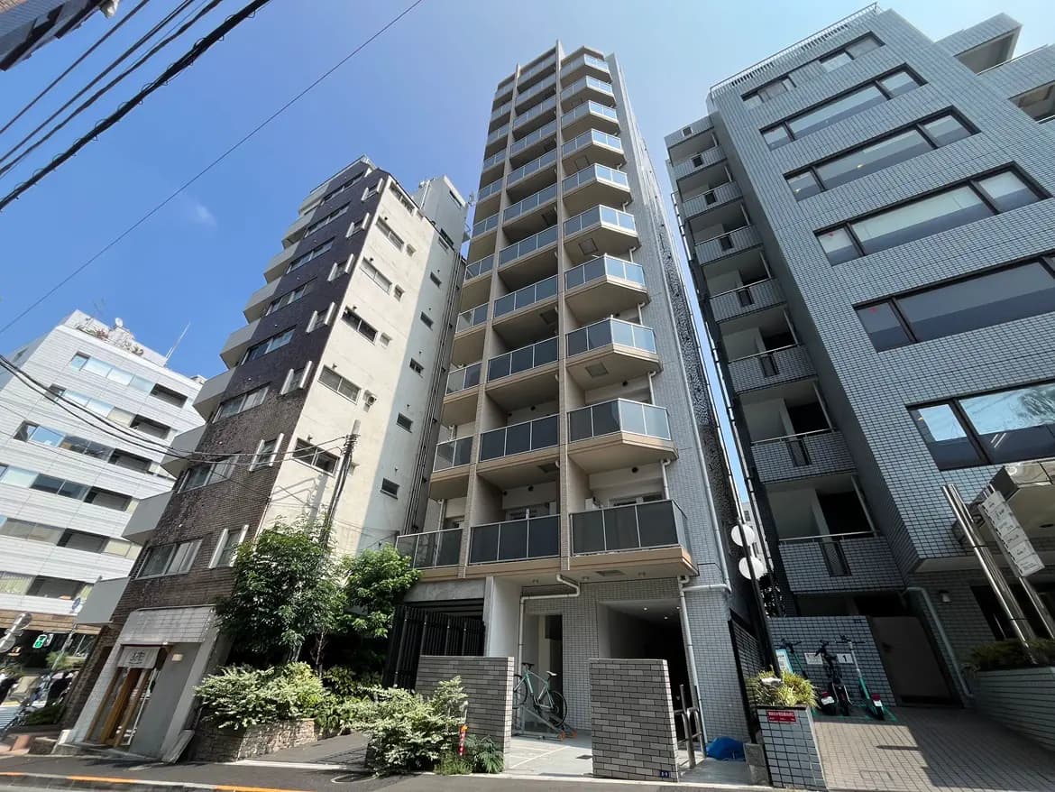 - 近代的な高層マンションの外観、周囲に他のビルが立ち並ぶ都市の風景、青空の下での写真