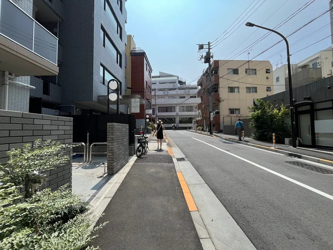 - 都市の住宅街の風景、マンションとレンガの建物が立ち並び、舗装された道路を歩く人々がいる様子