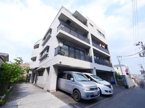 - モダンなデザインの4階建てのアパートメント、コンクリート外壁とバルコニー、駐車場に停まる2台の車があるエントランスの風景