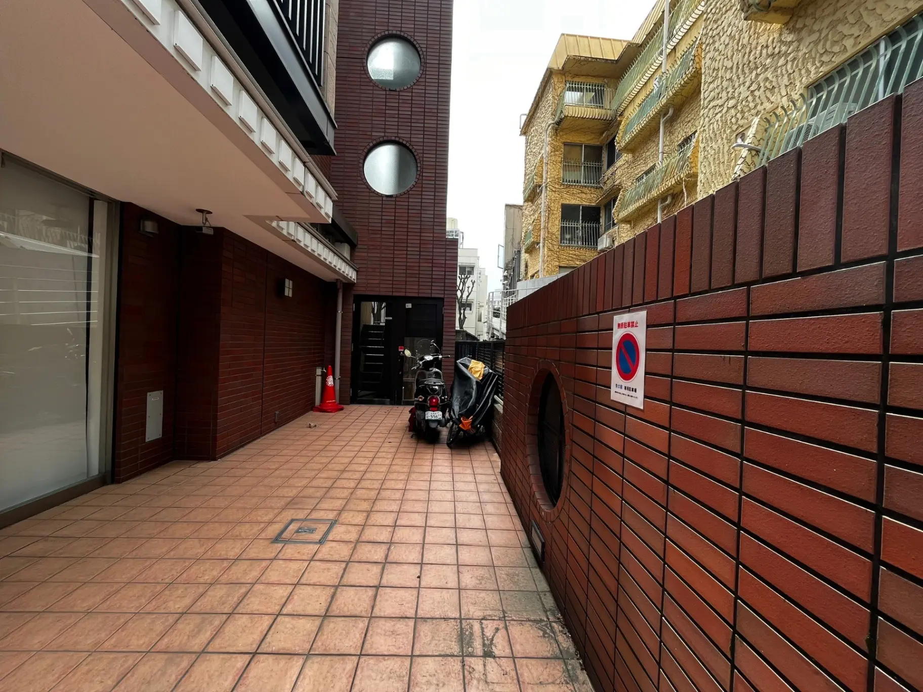 都会の狭い路地、レンガ造りの壁と禁止標識、バイクが駐車している光景