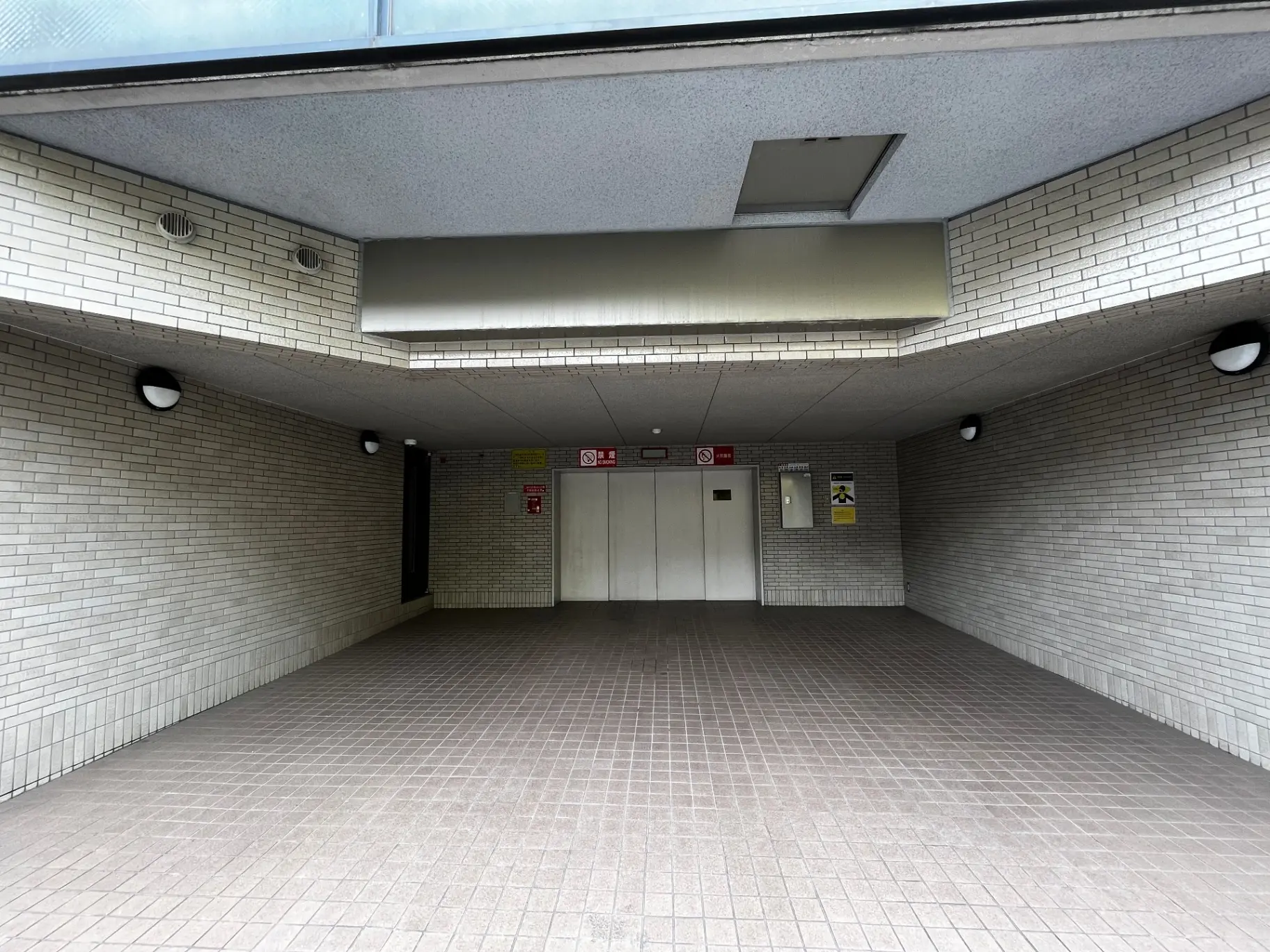 地下鉄の駅のエントランス、白いタイル壁と茶色のタイル床、照明付きの天井
