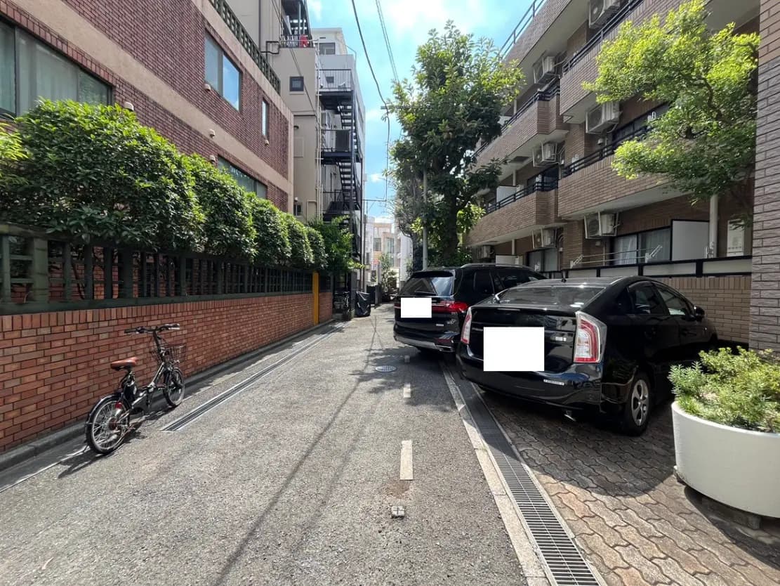 - 緑の生垣に囲まれた狭い道路、黒い車が並ぶ様子と、自転車が停められた街並み
