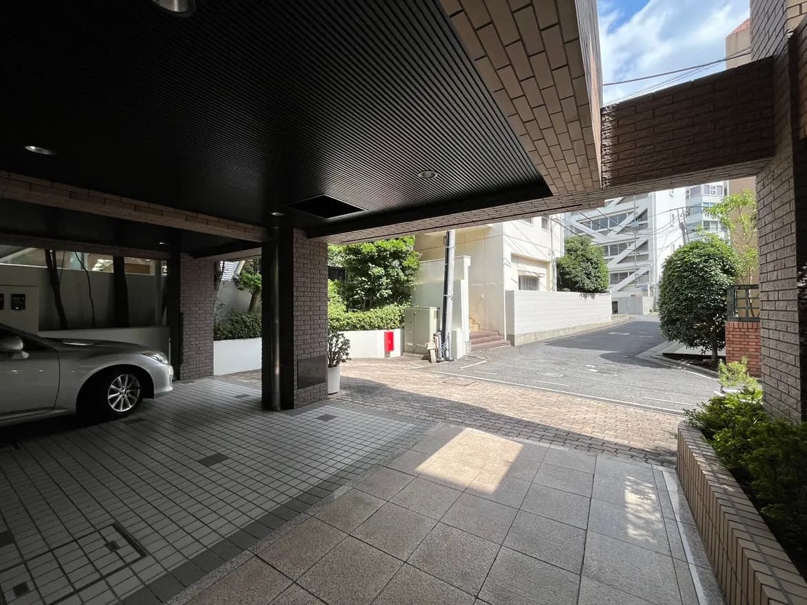 - シンプルでモダンな駐車場のエントランス、グレーのタイルとブロック造りの壁、緑豊かな植栽と明るい日の光が差し込む風景